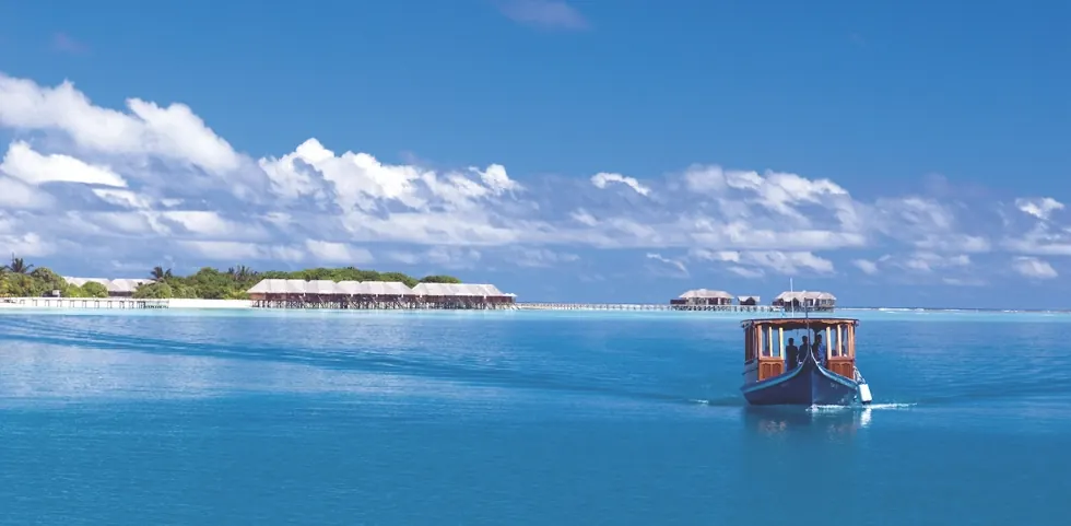 A boat crossing a turquoise lagoon towards overwater villas
